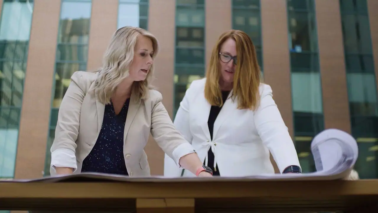 Two women review building plans in a glass lobby