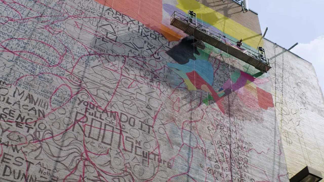 A mural of hand-drawn city maps being painted on a high wall